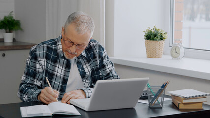 An elderly man keeps financial records at a computer.