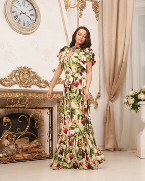 Elegant lady in green sundress with floral design standing and posing in bright room interior. Full length portrait