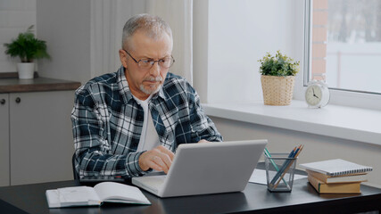 An elderly man keeps financial records at a computer.