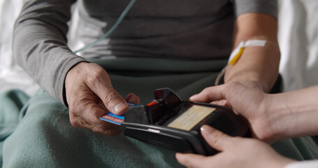 Male patient with intravenous drip using credit card paying for health insurance in hospital ward