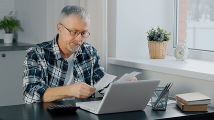 An elderly man keeps financial records at a computer.