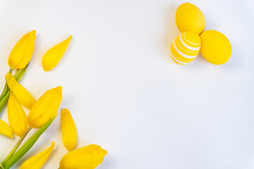 Easter composition with a bouquet of tulips and yellow eggs on a white background. View from above. Minimal easter concept. Space for text.
