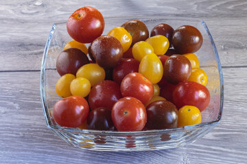 Multicolored tomatoes of different varieties in a glass bowl. Fashionable vegan food.