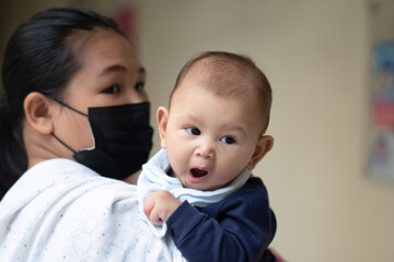 Asian Baby Girl Yawning while being held by mother wearing a mask during pandemic