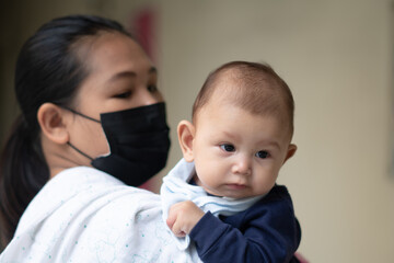 Asian Baby Girl Wants to go in one direction while being held by mother wearing a mask during pandemic