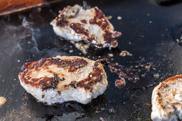 Marinated boneless pork chops cooking on a hibachi style outdoor large griddle