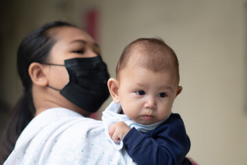 Asian Baby Girl Wants to go in one direction while being held by mother wearing a mask during pandemic
