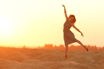 Elegant woman with long hair in long dress dancing elegant on sand in desert. Sunrise, backlight photo