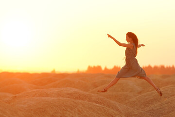 Elegant woman in long dress with straw hat junping elegant on sandy hills in desert. Sunrise, backlight photo