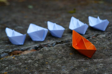 A group of paper boats. Ahead is an orange-colored boat. There's a crack in the concrete between them.