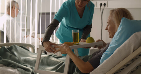 Nurse serving senior female patient meal in hospital bed