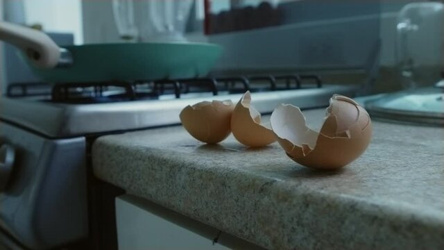Frying eggs in a green frying pan on the gas stove. Egg shells on the counter