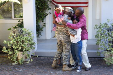 African american soldier father hugging wife, children and father in front of their house