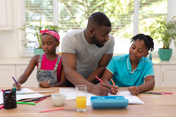 African american father sitting at table helping son and daughter with school work