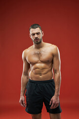 Fototapeta na wymiar Strong athlete posing at the photo camera in black sportswear isolated on red background