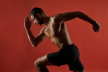 Strong athlete with powerful torso in action isolated on red background of a studio