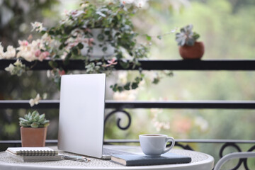 Coffee cup and laptop and notebook on white metal table at balcony