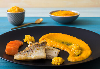 Baked fillet of zander, carrot-ginger puree and orange caviar. Blue wooden table, no people.