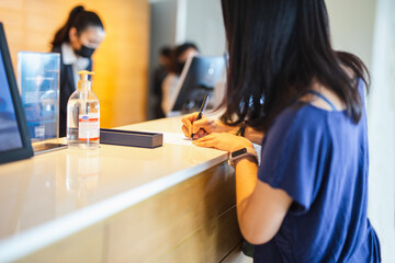Woman guest signing bill at hotel reception.