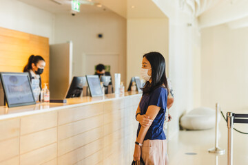 Tourist woman and receptionist at hotel counter wearing medical mask against virus.