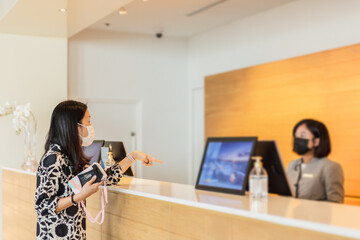 Woman hotel guest and receptionist at hotel counter wearing medical mask against virus.