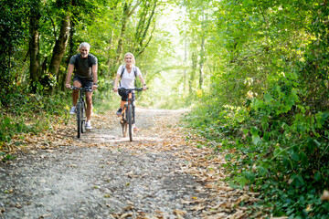 Portrait of smiling mature couple riding bicycles on footpath in forest