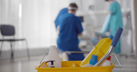 Focus on bucket with detergents and nurse team cleaning ward in hospital on blurred background