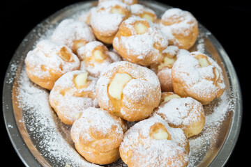Cream puffs stuffed with custard isolated on black background. Selective focus
