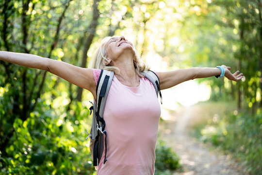 Smiling mature woman stretching arms while standing in forest