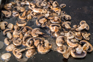 sauteed mushroom slices on an outdoor griddle propane grill in the summer
