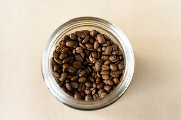 roasted coffee beans in glass jar, top view, circle shape on beige background