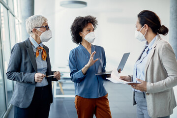 Team of businesswomen wearing face masks while discussing and working at corporate office.
