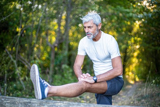 Mature man stretching his leg in forest