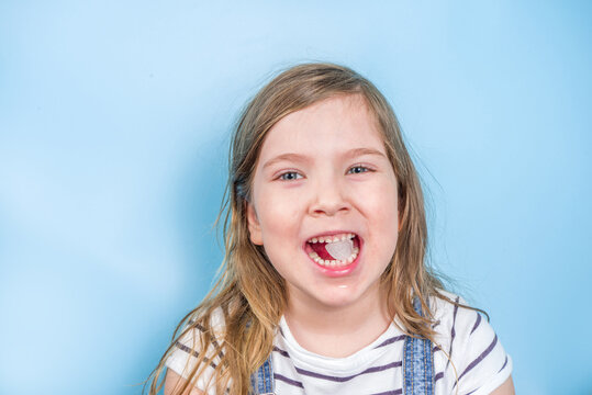 Cute toddler preschool girl eating an ice cube on a light blue background. Joyful girl with a piece of ice in her mouth.