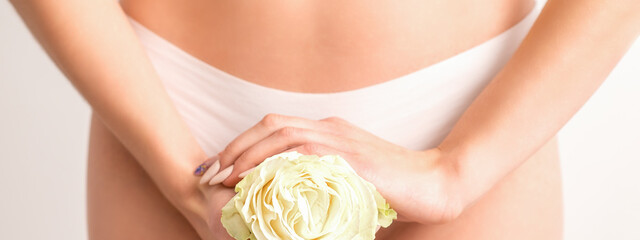 Young woman's hands holding a white flower covering epilate bikini zone isolated on white studio background. Concept of female health, reproductive, gynecology - obrazy, fototapety, plakaty