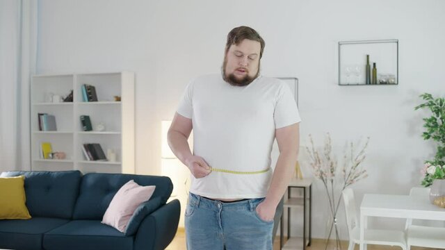 Unhappy chubby male looking at measuring tape, belly fat, risk of obesity, diet