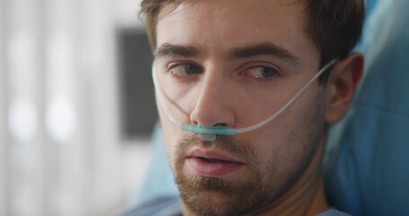 Upset man lying with oxygen nasal catheter on face preparing for surgery