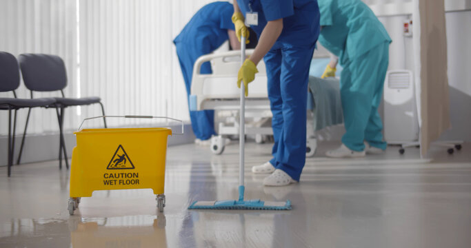 Nurses mopping floor and making bed in empty hospital ward