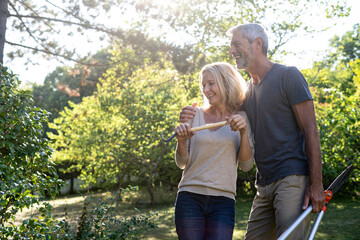 Cheerful mature couple with gardening equipment standing in backyard