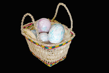 Easter eggs in a wicker basket with handles. Easter still life, isolated on black. Selective focus