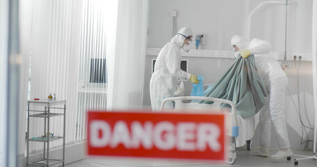 Medical staff in ppe suit putting bedsheets in anti-virus protection package disinfecting...
