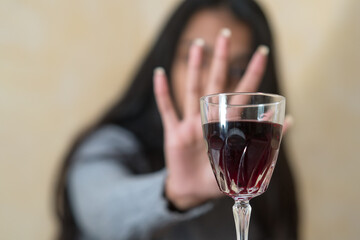 Giving up alcohol. A young woman at the table refuses with her hand a glass of red wine. Selective focus