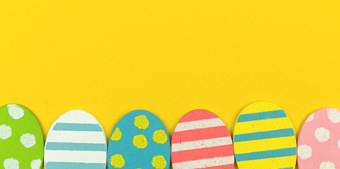 Colorful easter eggs bottom border on a yellow background, banner, copy space and top view, flat lay design