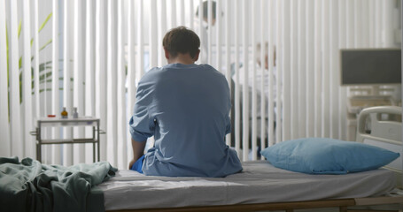 Back view of young desperate man sitting at hospital bed alone