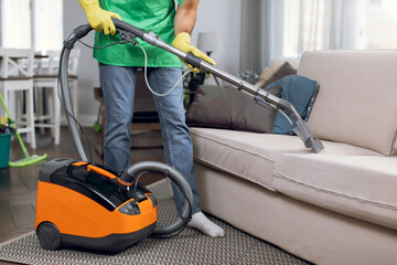 Close up of male janitor doing cleanup of couch with vacuum