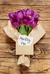 Bouquet and MARRY ME card on wooden table
