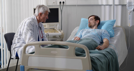 Obraz premium Hospitalized man lying in bed talking to senior doctor