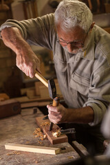Experienced senior carpenter working in his workshop.Carving and working with chisel.
