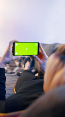 Young woman lying on a couch and using smartphone with horizontal green screen. High quality photo