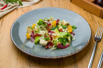 salad with orange, Parma ham and cheese on grey plate on wooden table